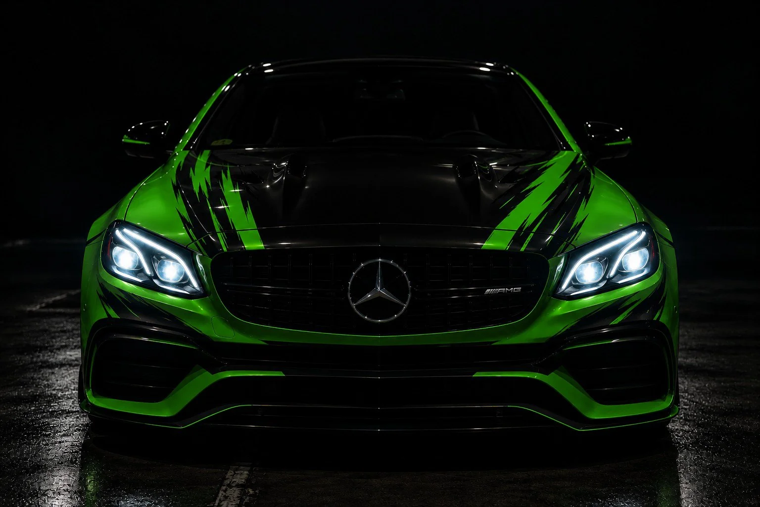 Mașină sport verde cu grafică neagră, în întuneric, cu farurile aprinse